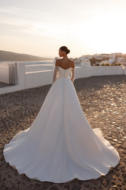 Back view of an ivory wedding dress with sheer lace sleeves, a center row of buttons, and a wide train