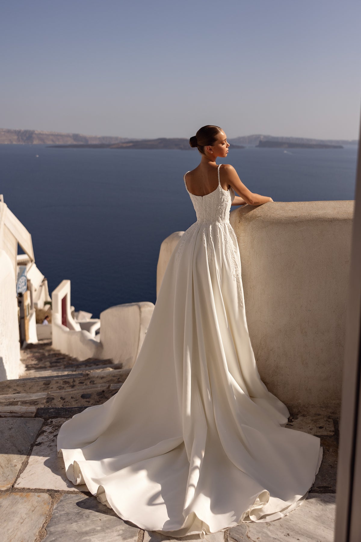 Back of an ivory wedding dress showing a low scoop back, lace bodice, thin straps, and long train