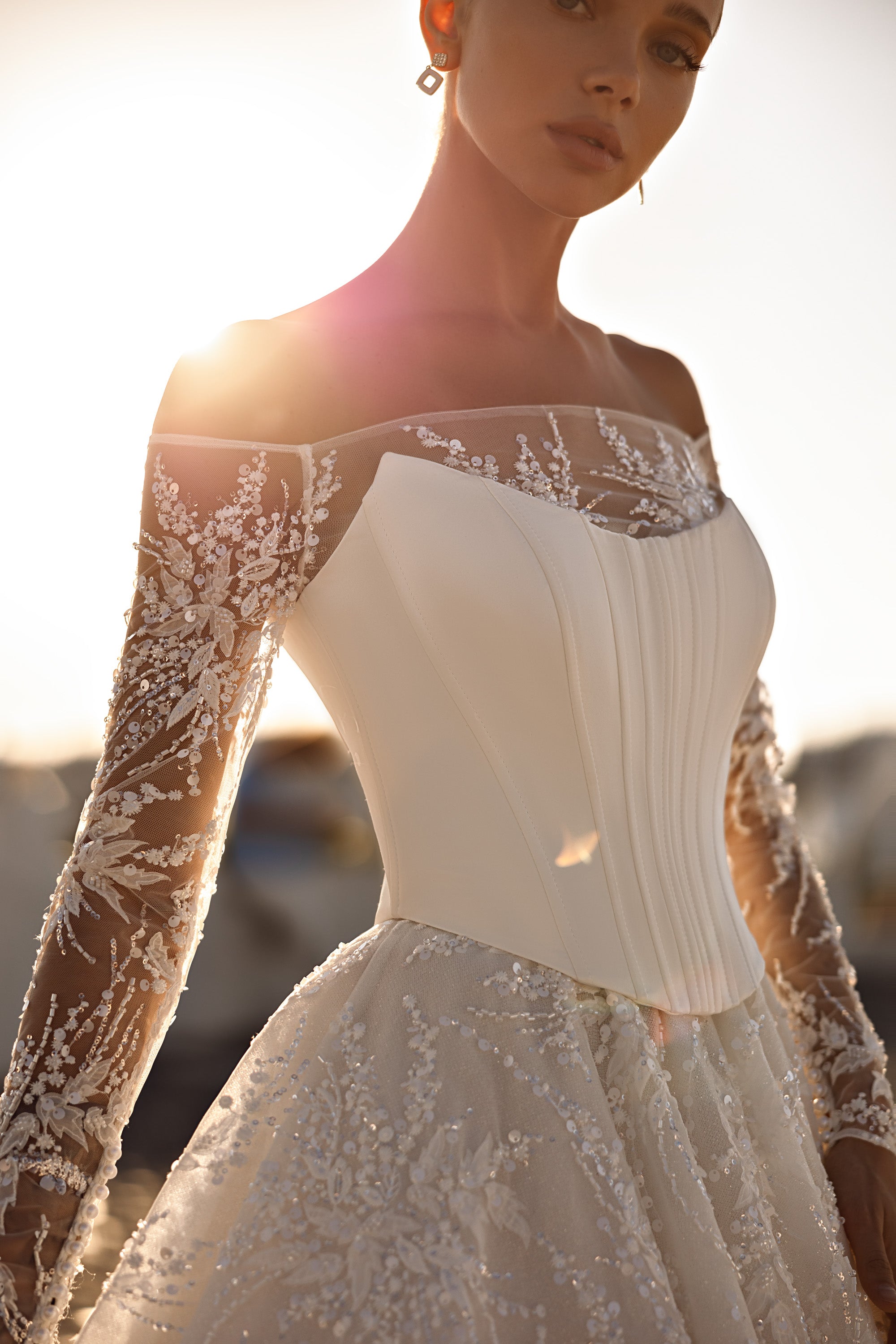 Close-up of an ivory wedding dress bodice with vertical seams, sheer lace neckline, and floral lace sleeves