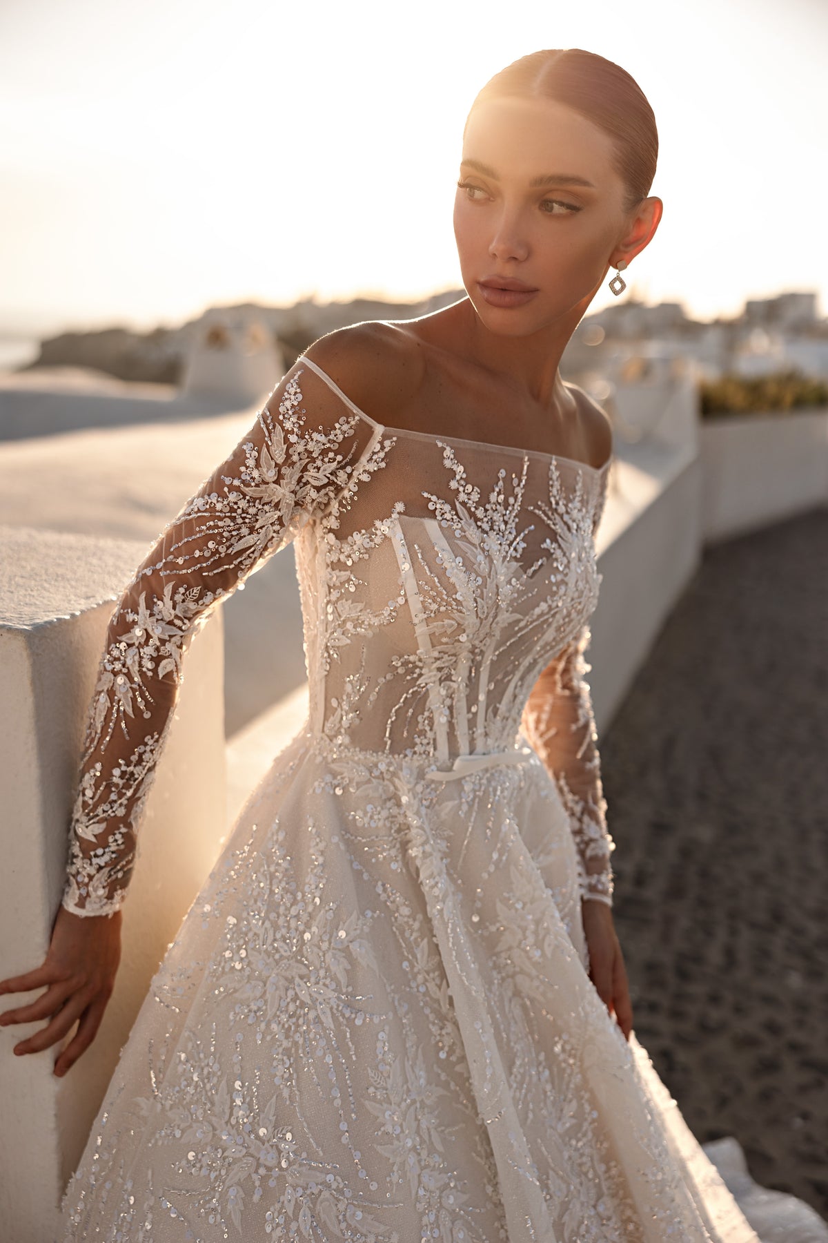 Close-up of an ivory wedding dress with floral lace appliqués, sheer long sleeves, and an off-shoulder neckline