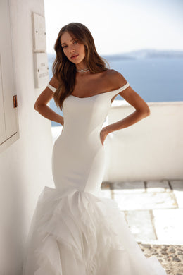 Ivory mermaid wedding dress with an off-the-shoulder neckline and dramatic layered ruffled skirt