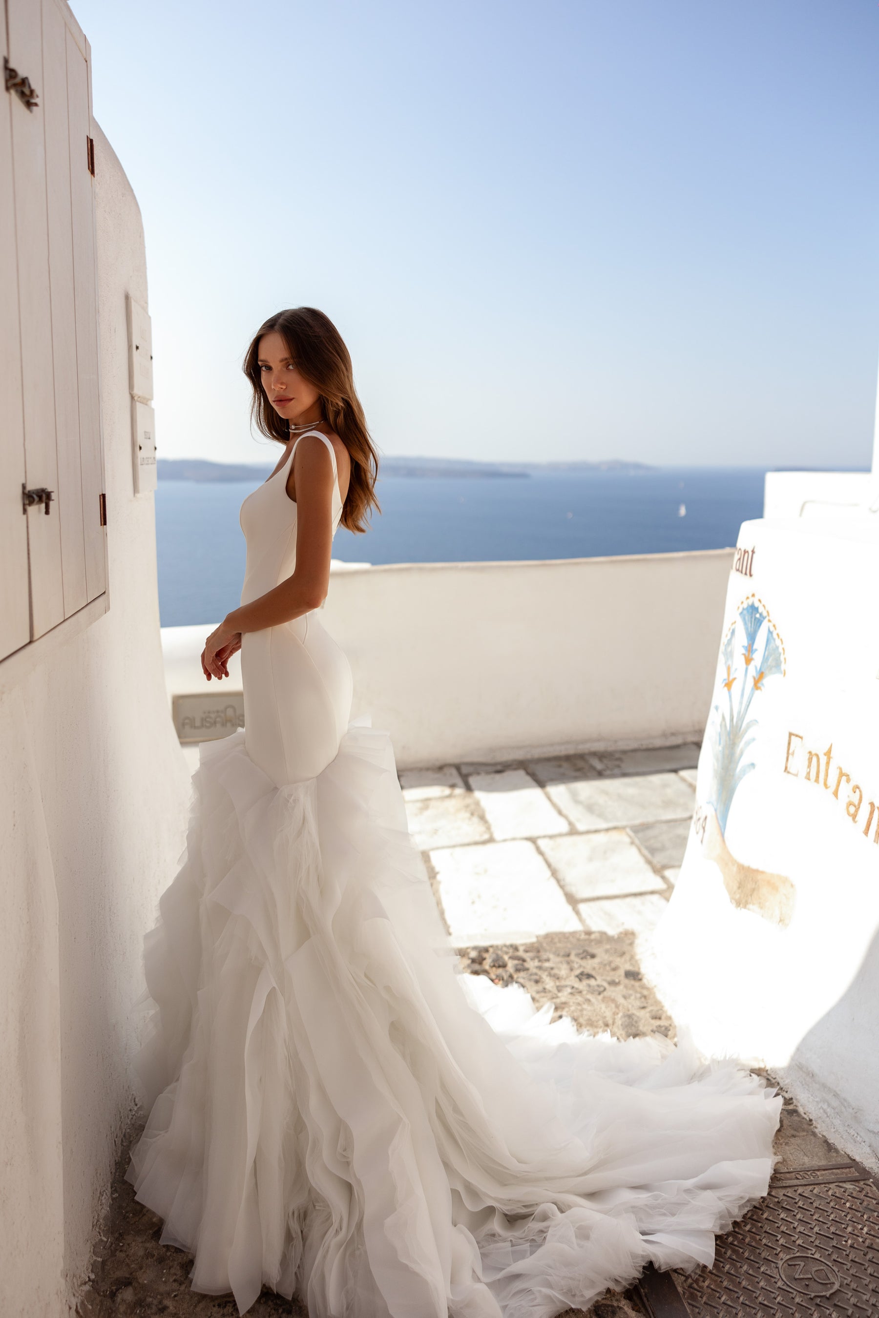 Side profile of an ivory mermaid wedding dress with a fitted waist, layered ruffles, and long train