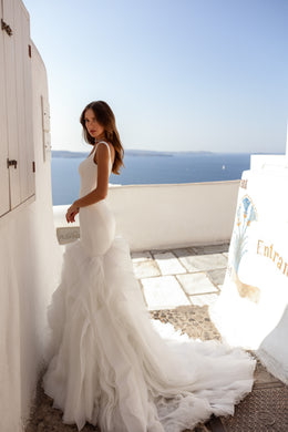 Side profile of an ivory mermaid wedding dress with a fitted waist, layered ruffles, and long train