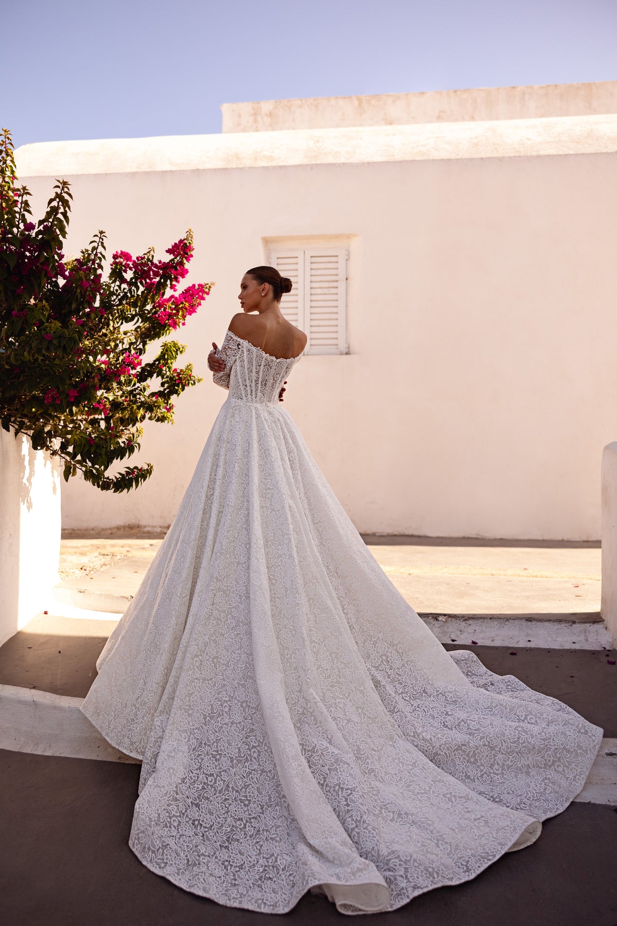 Ivory lace wedding dress with a sweeping ball gown skirt, long train, and off-the-shoulder sleeves from behind