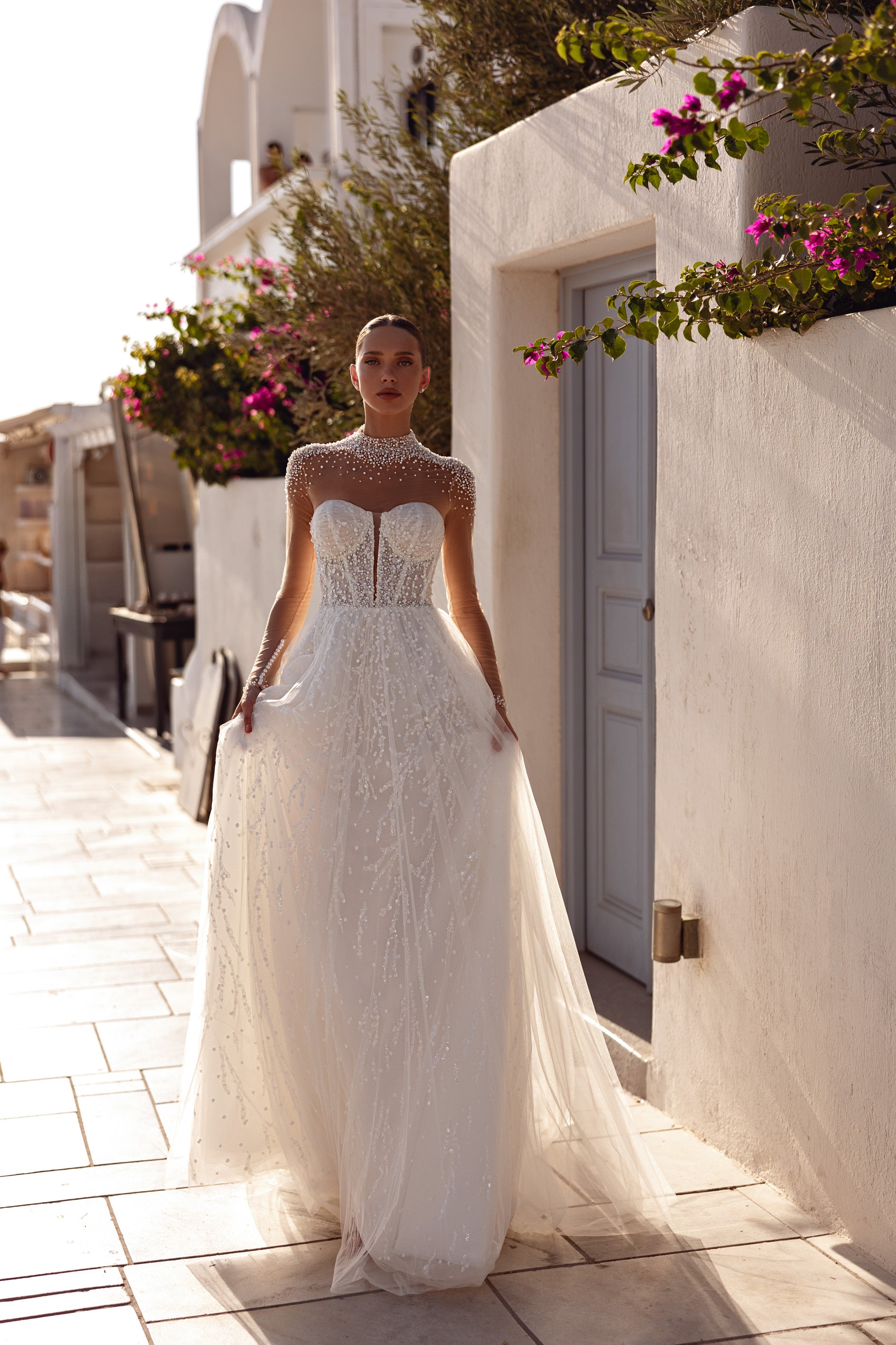 Ivory A-line wedding dress with a sheer pearl-beaded high neckline, long sleeves, and flowing train