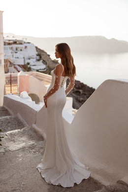 Ivory wedding dress showing a fitted back with lace-up detailing, sheer lace sleeves, and a train