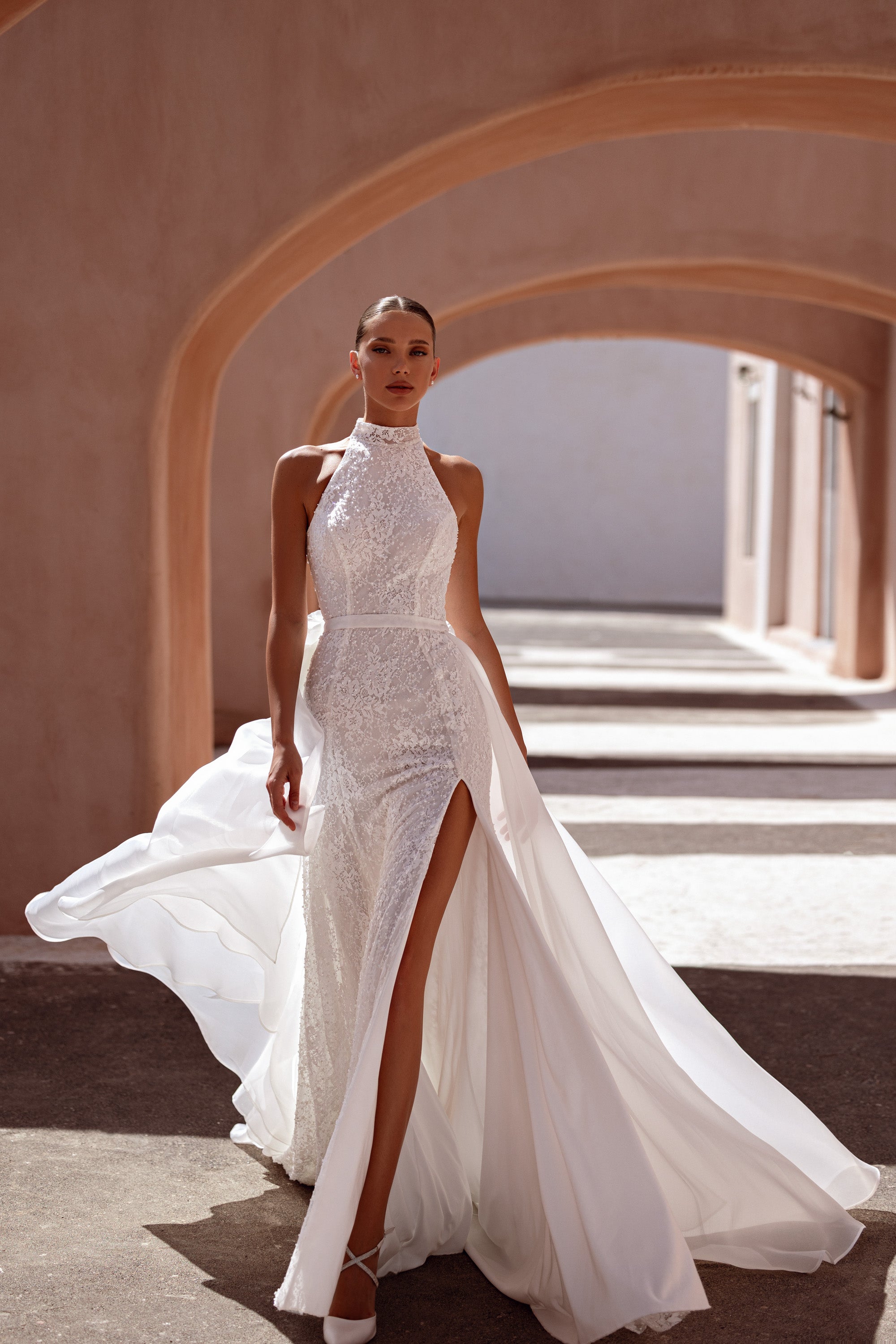 Ivory wedding dress with a high halter neckline, sparkling lace sheath, thigh-high slit, and flowing overskirt