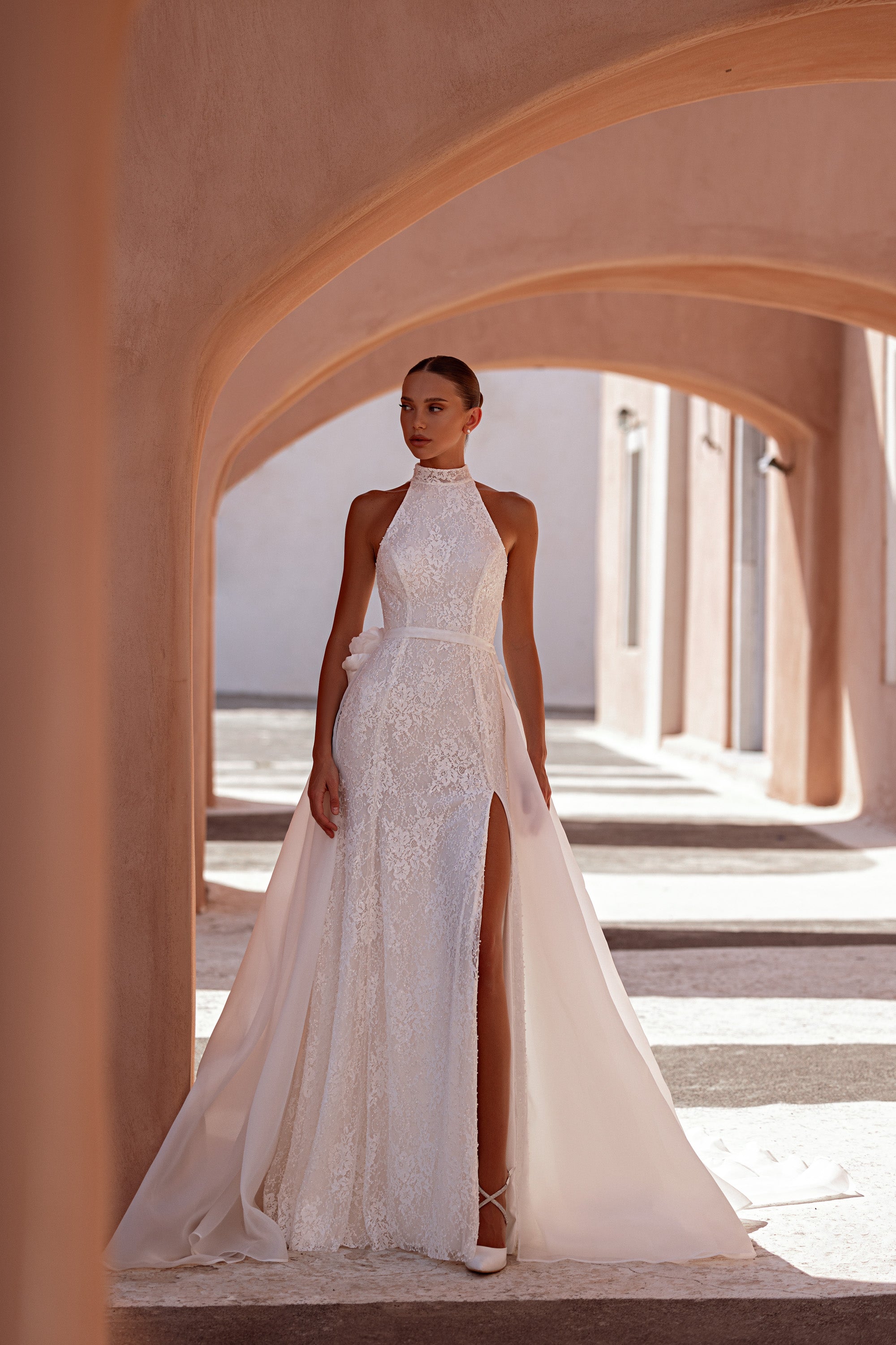 Fitted ivory wedding dress with a high halter neckline, lace bodice, thigh-high slit, and long overskirt
