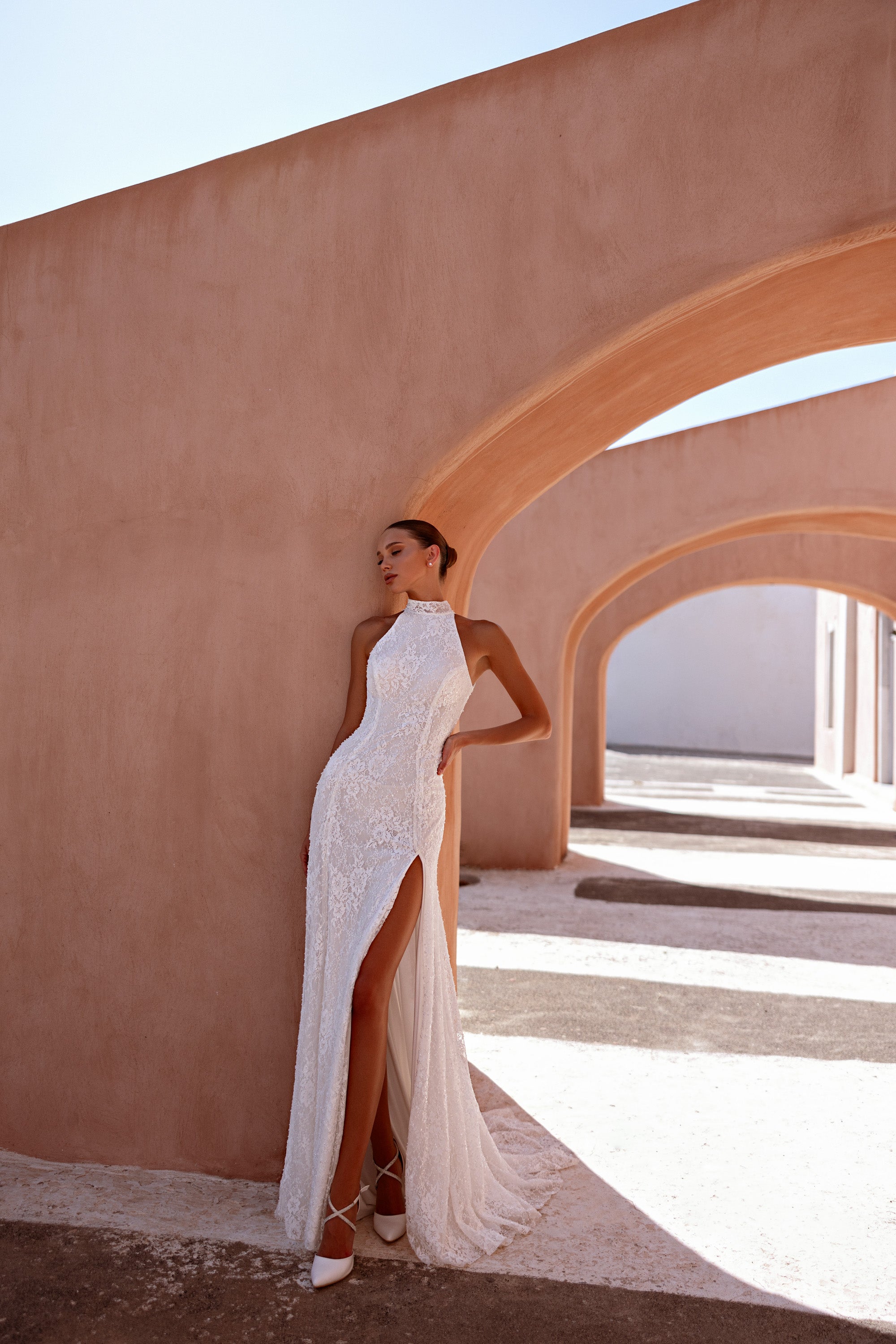Side view highlights the fitted lace sheath, dramatic thigh-high slit, and sheer overskirt of an ivory wedding dress