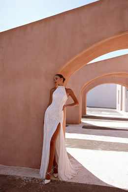 Side view highlights the fitted lace sheath, dramatic thigh-high slit, and sheer overskirt of an ivory wedding dress