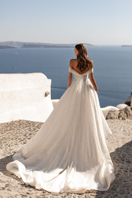 Ivory wedding dress showing an embellished back, off-the-shoulder sleeves, and a long flowing train