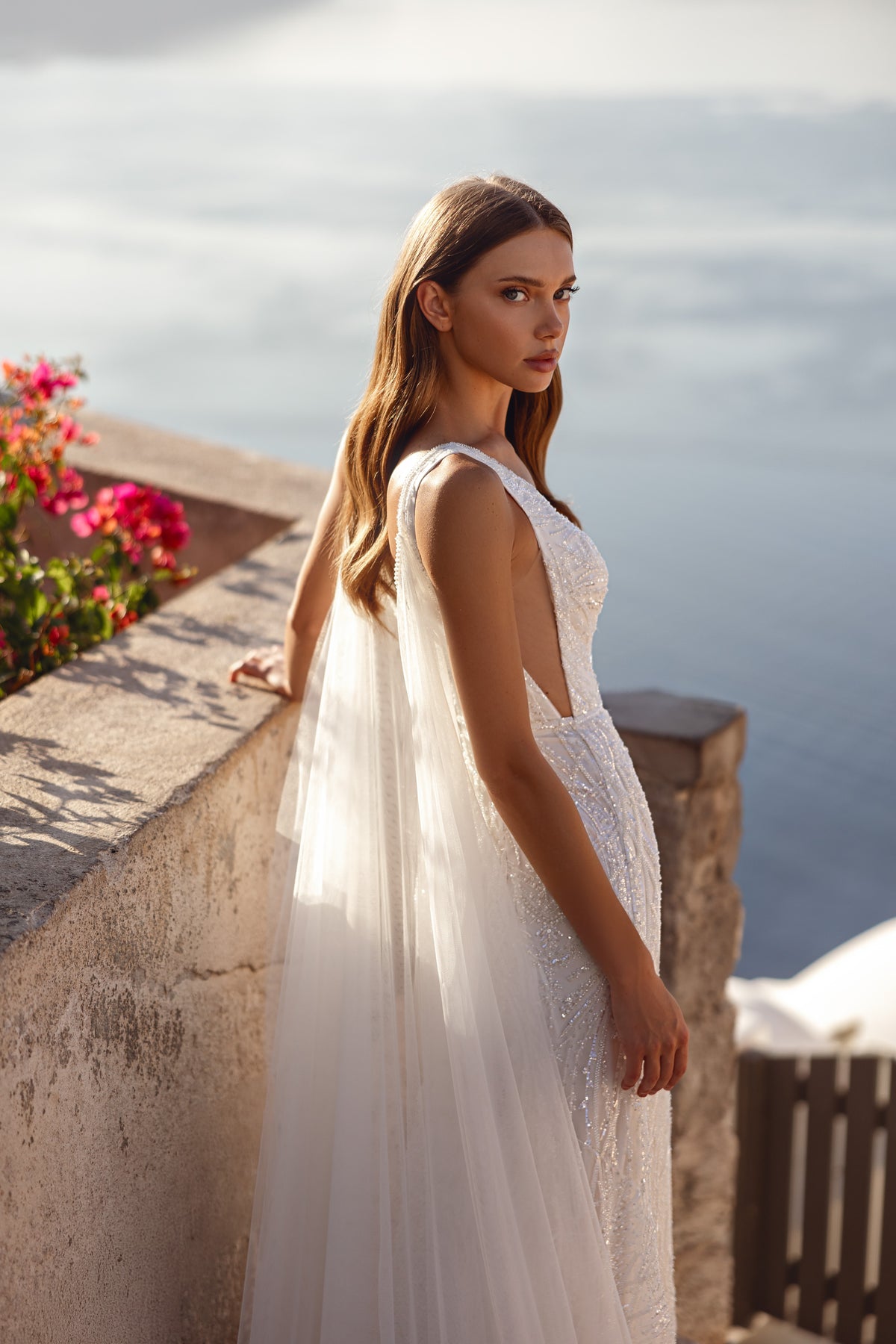 Side view of a sparkling sheath wedding dress with a sheer flowing cape and V-neckline