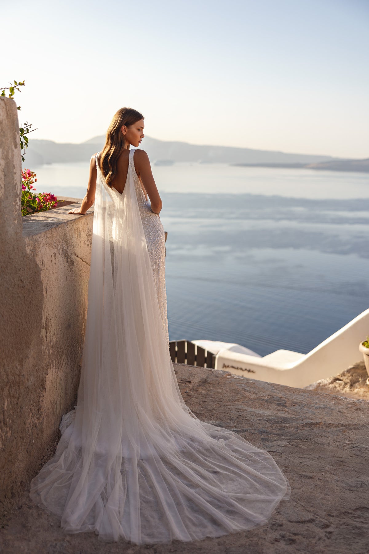 Open V-back wedding dress with a sheer cape and long, flowing train