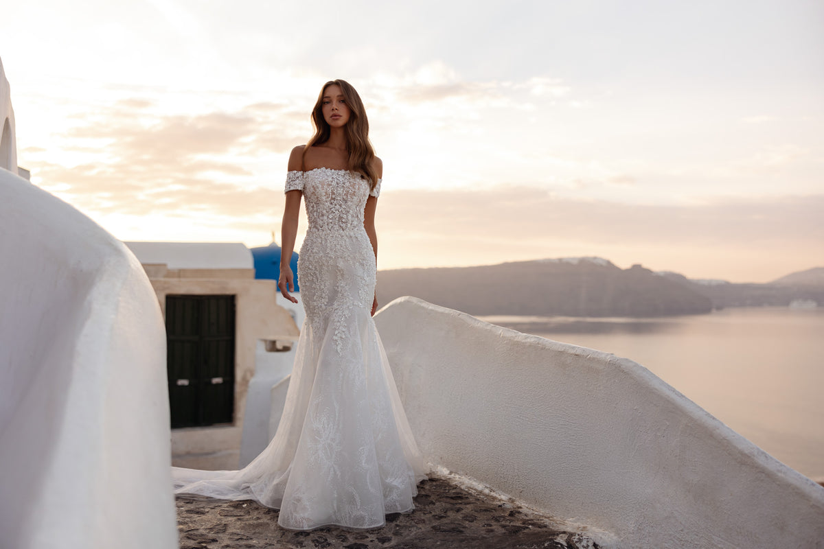 Fitted ivory wedding dress with sparkling lace, off-the-shoulder sleeves, and a flared mermaid hem