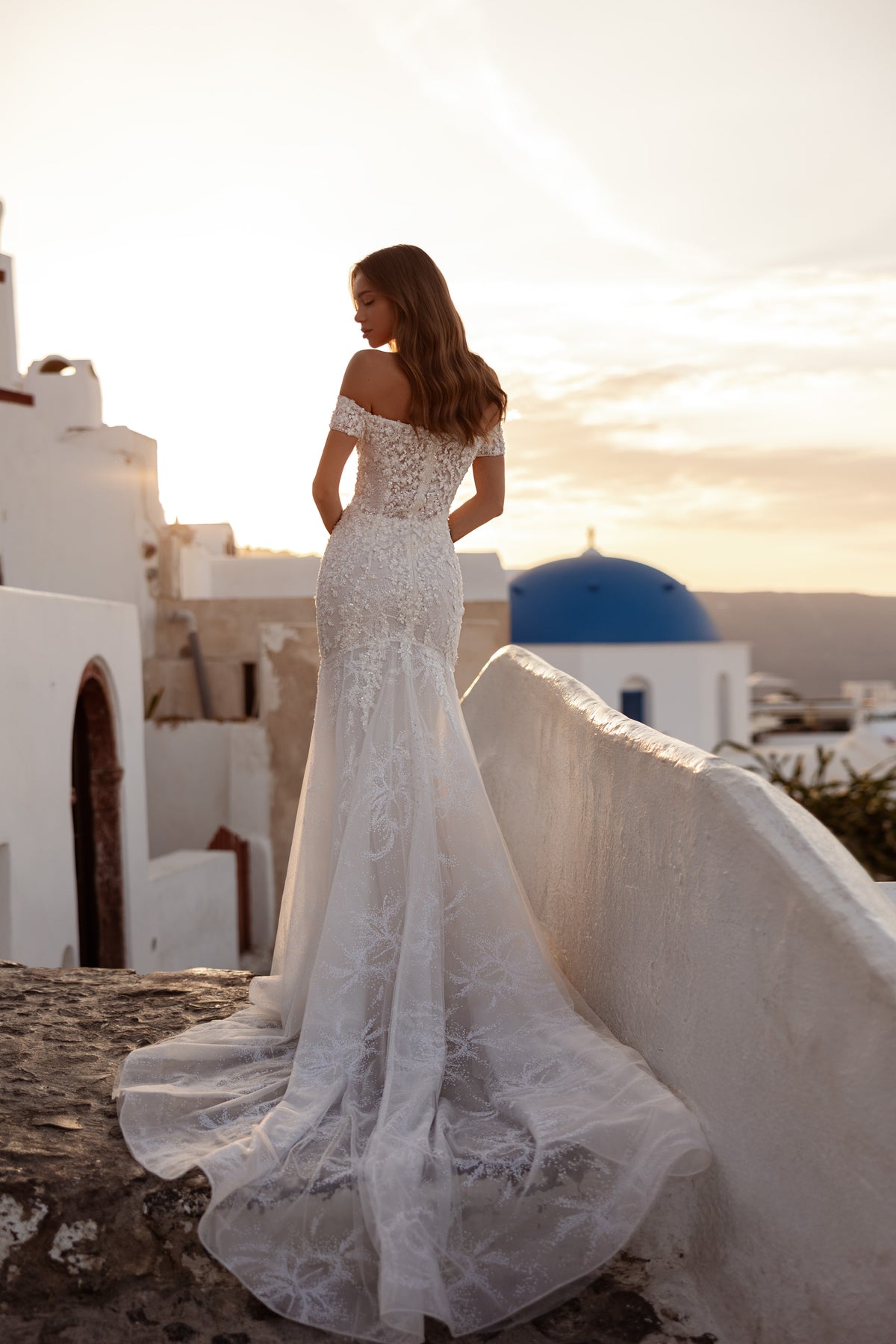 Lace-covered back of an ivory mermaid wedding dress with off-the-shoulder sleeves and a long train