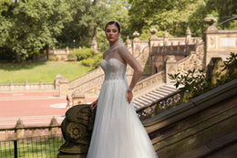 Ivory wedding dress with a beaded illusion neckline, sweetheart bodice, sheer sleeves, and glittering A-line skirt