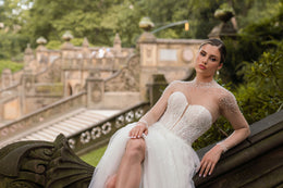 Sweetheart ivory wedding dress with a pearl-detailed illusion neckline, sheer sleeves, and visible skirt slit