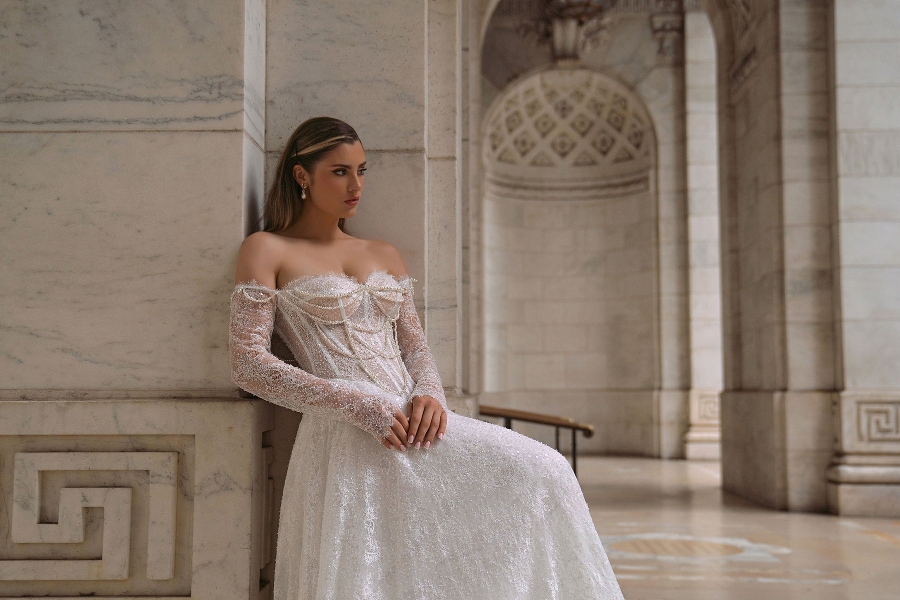 Beaded ivory wedding dress with an off-the-shoulder neckline, long sheer lace sleeves, and a flowing full skirt