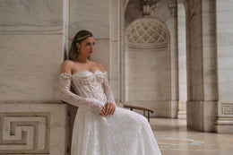 Beaded ivory wedding dress with an off-the-shoulder neckline, long sheer lace sleeves, and a flowing full skirt