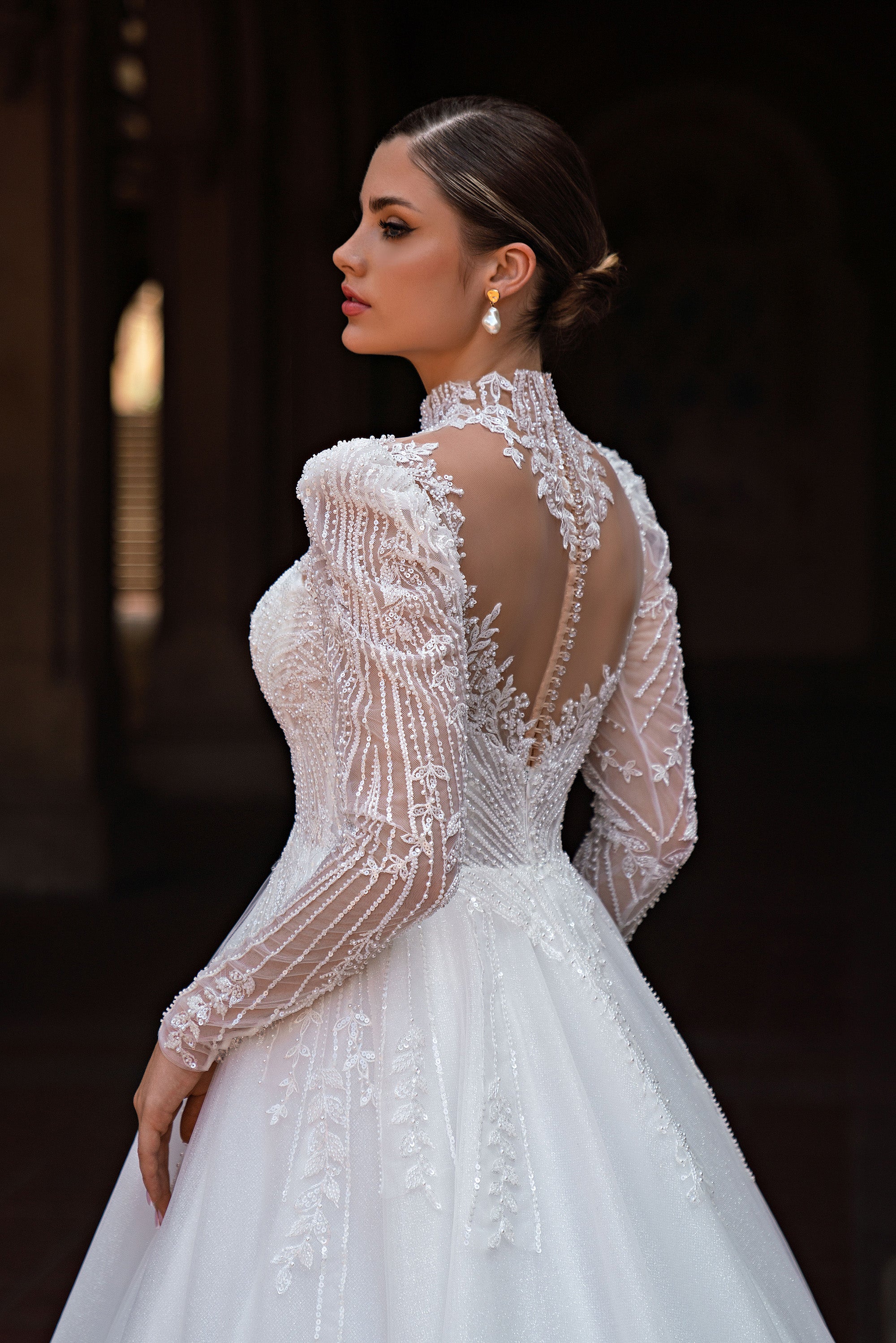 Back detail of a white wedding dress with a sheer beaded lace back, high neck, and long sleeves