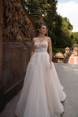 Ivory A-line wedding dress with thin straps, embellished bodice, floral appliqués, and a flowing skirt