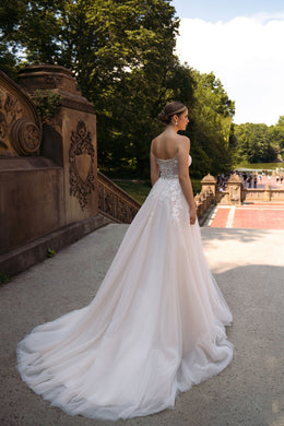 Back view of an ivory wedding dress with thin straps, floral appliqués, and a long flowing train