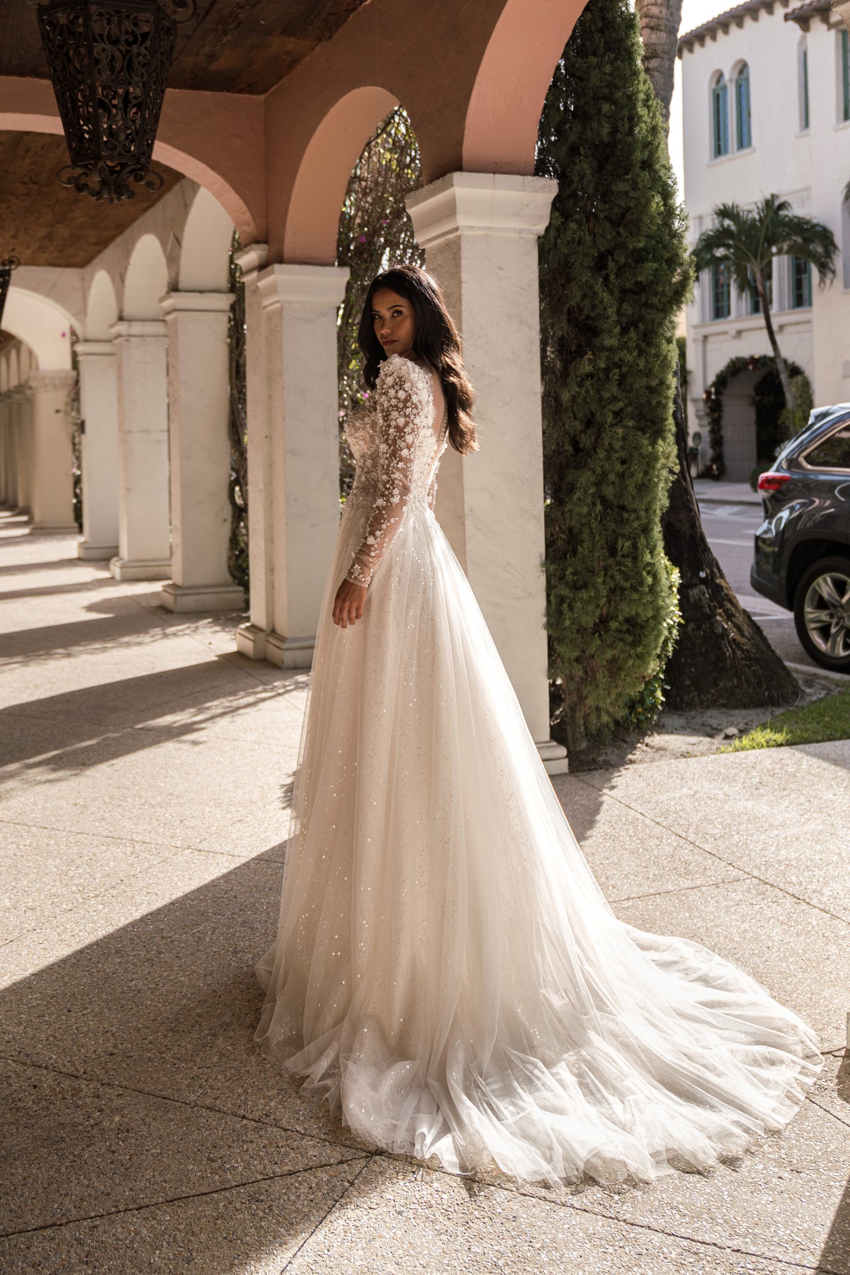 Ivory A-line wedding dress shown from the side with sheer lace sleeves, a flowing skirt, and a long train