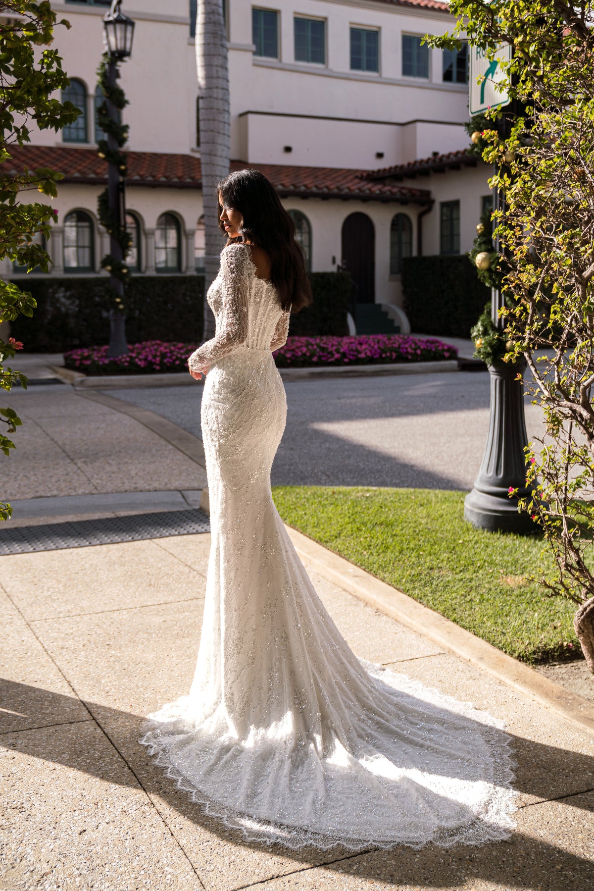 Side profile of an ivory wedding dress with a fitted mermaid silhouette, long lace sleeves, and trailing train
