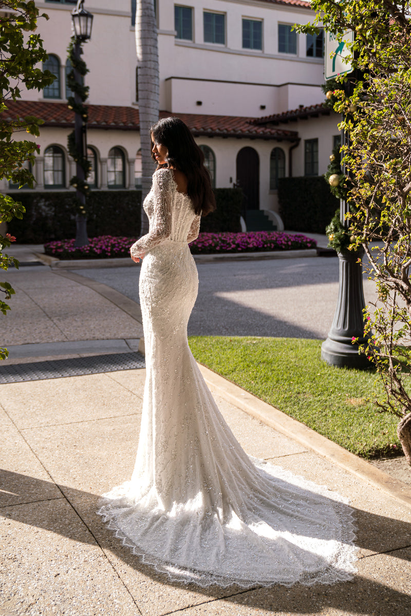 Side profile of an ivory wedding dress with a fitted mermaid silhouette, long lace sleeves, and trailing train