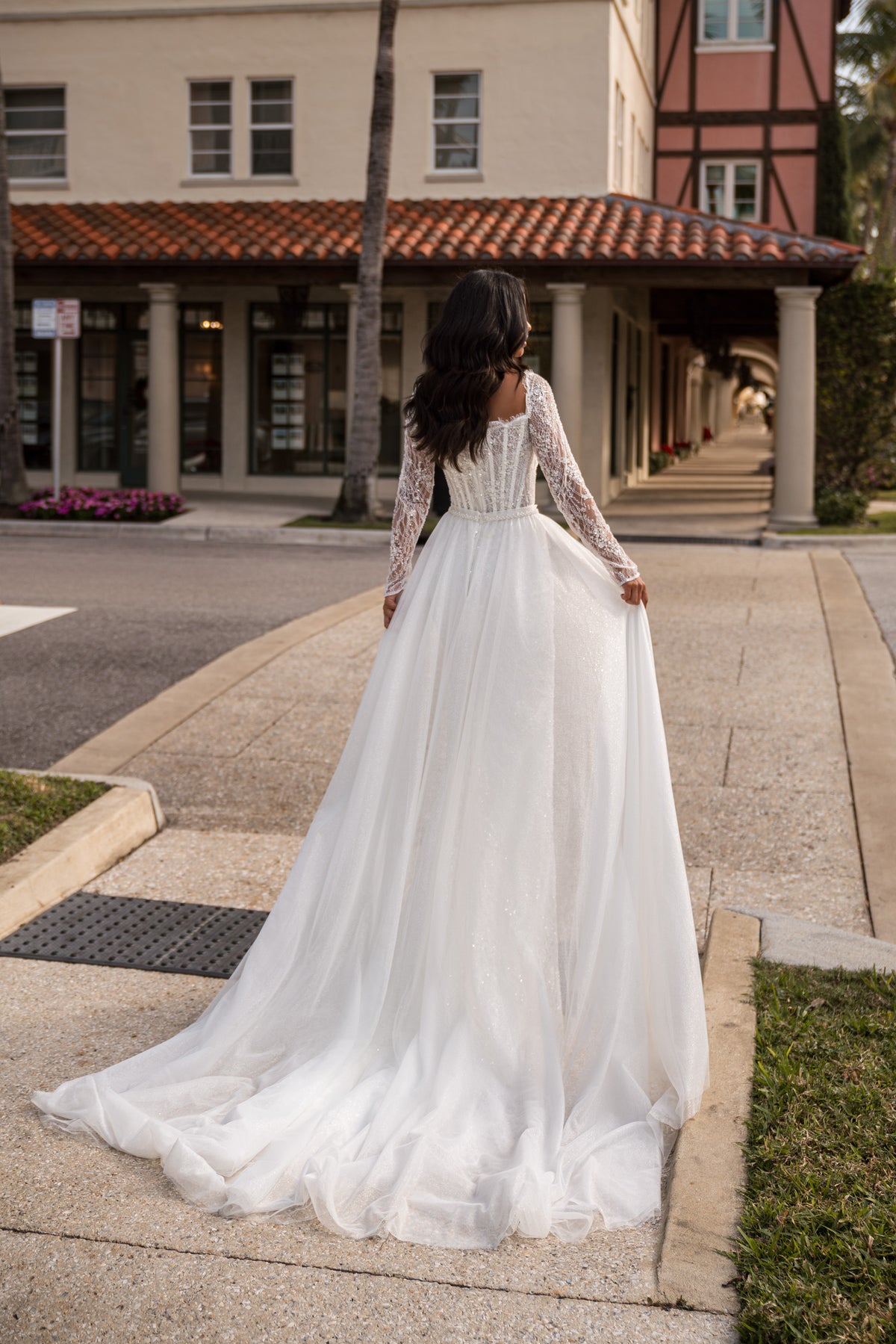Back of an ivory wedding dress with long lace sleeves, a fitted waist, and a full sheer train