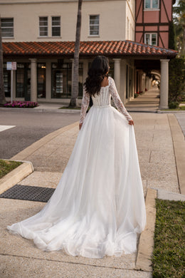 Back of an ivory wedding dress with long lace sleeves, a fitted waist, and a full sheer train