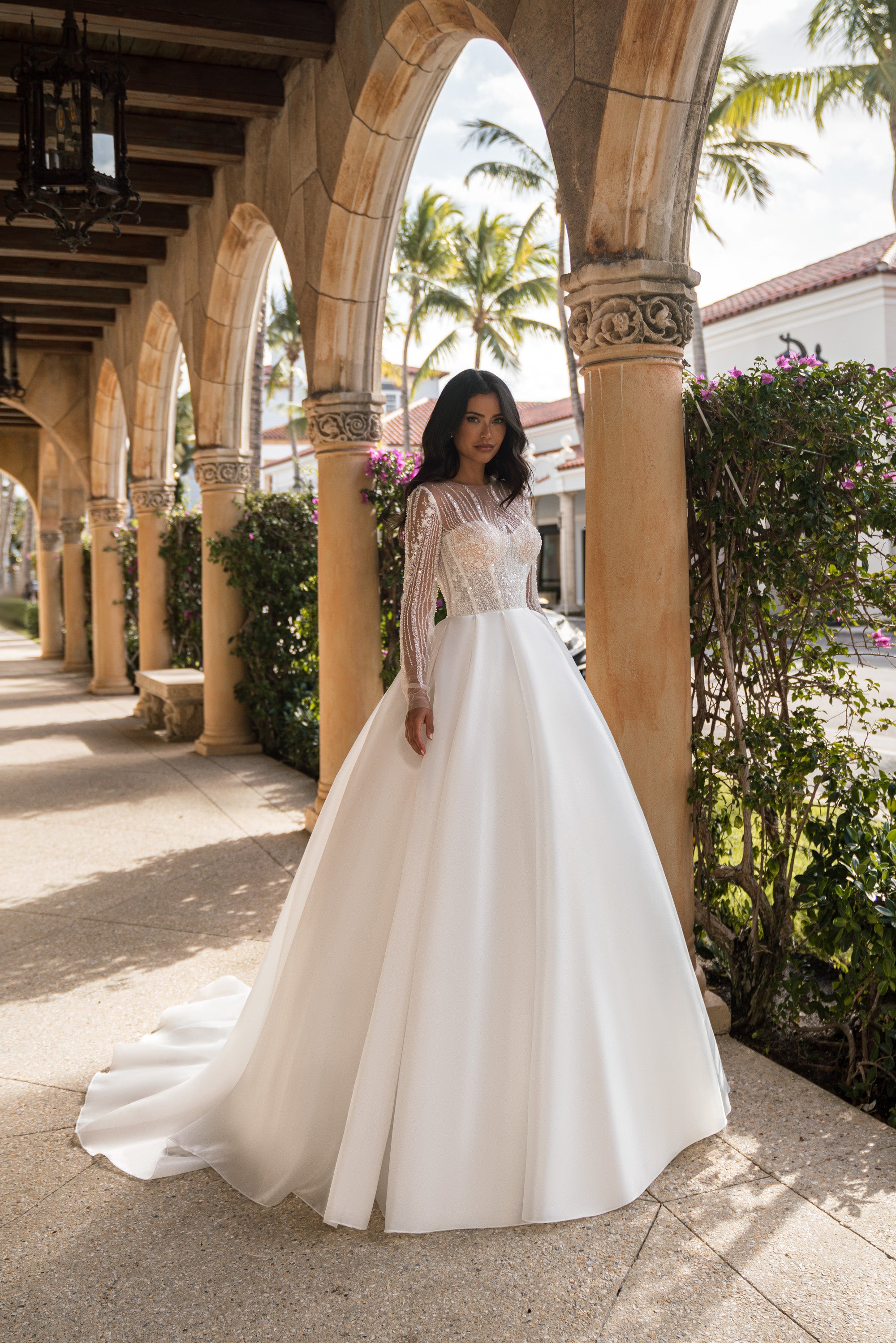 Ivory ball gown wedding dress with a beaded illusion bodice, long sheer sleeves, and a sweeping train