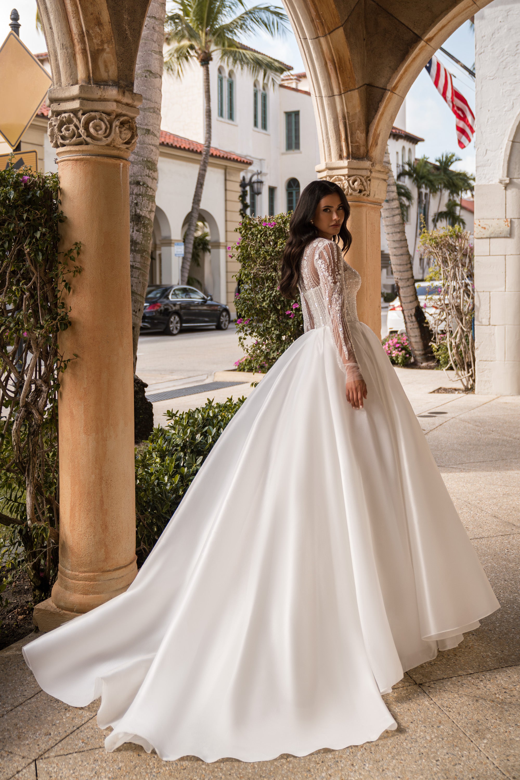 Flowing ivory wedding dress with a full skirt, sheer embellished sleeves, and a long trailing train