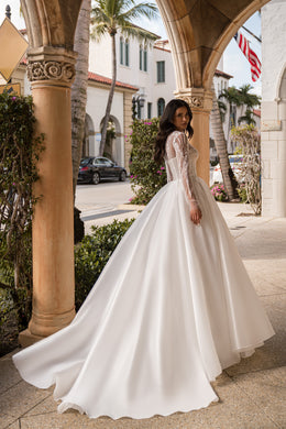 Flowing ivory wedding dress with a full skirt, sheer embellished sleeves, and a long trailing train