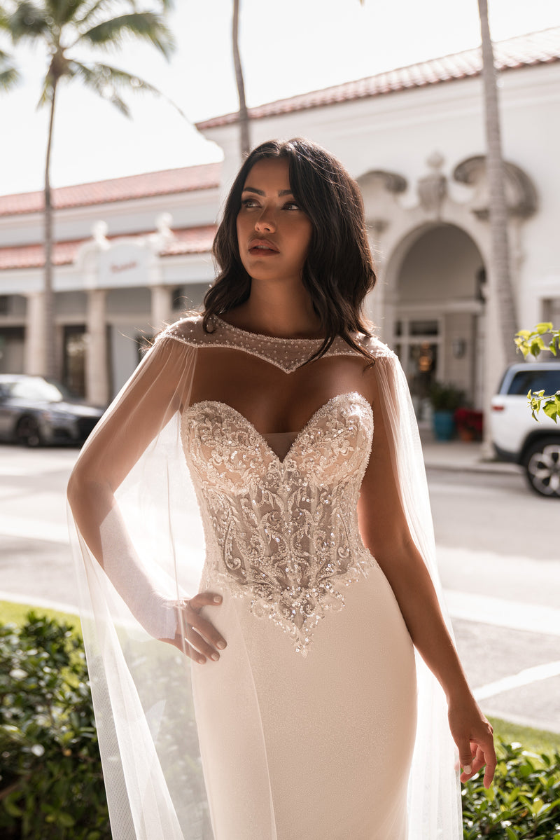 Ivory mermaid wedding dress with a sweetheart neckline, sparkling lace bodice, and sheer cape sleeves