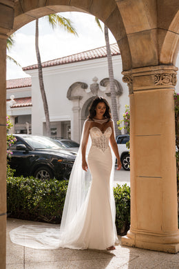 Full-length ivory mermaid wedding dress with a sparkling lace bodice, sheer cape, and sweeping train