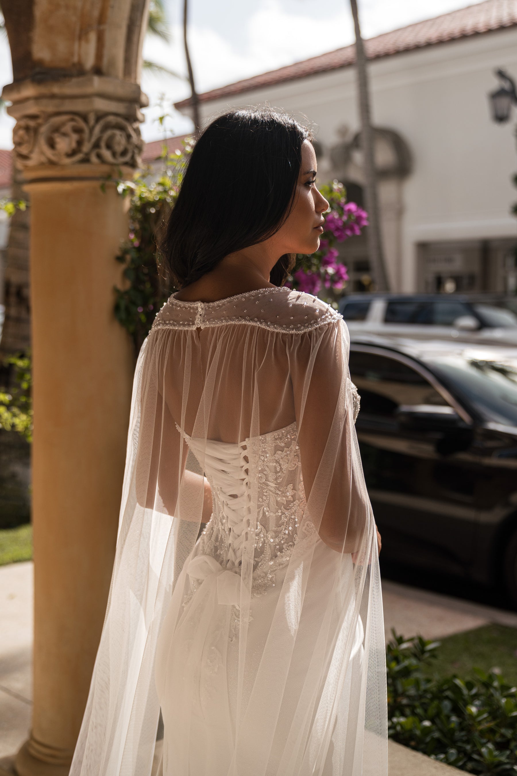 Sheer cape draped over the embellished back of an ivory mermaid wedding dress