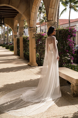 Side view of an ivory wedding dress with a long sheer cape and extended train