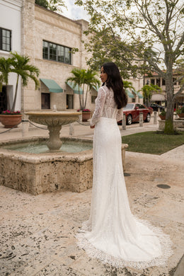Side view of an ivory sheath wedding dress showing its long lace sleeves and extended trailing train
