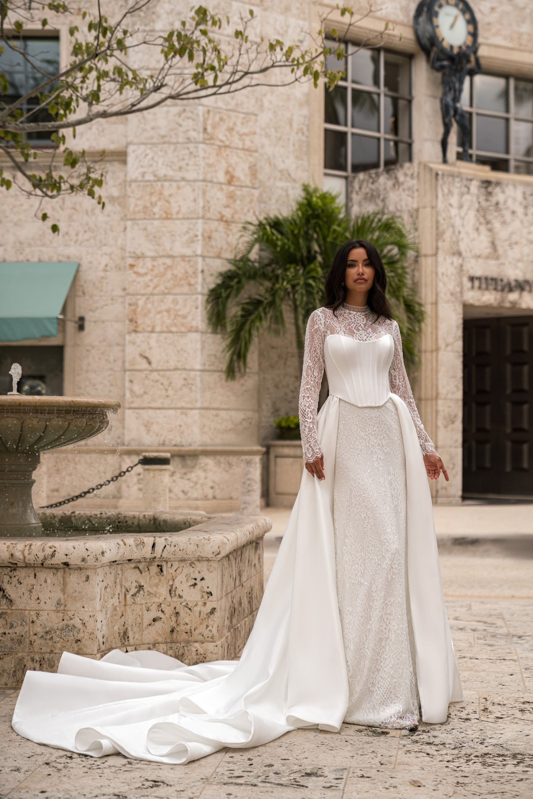 Ivory wedding dress with a fitted lace skirt, long lace sleeves, and a detachable overskirt with train