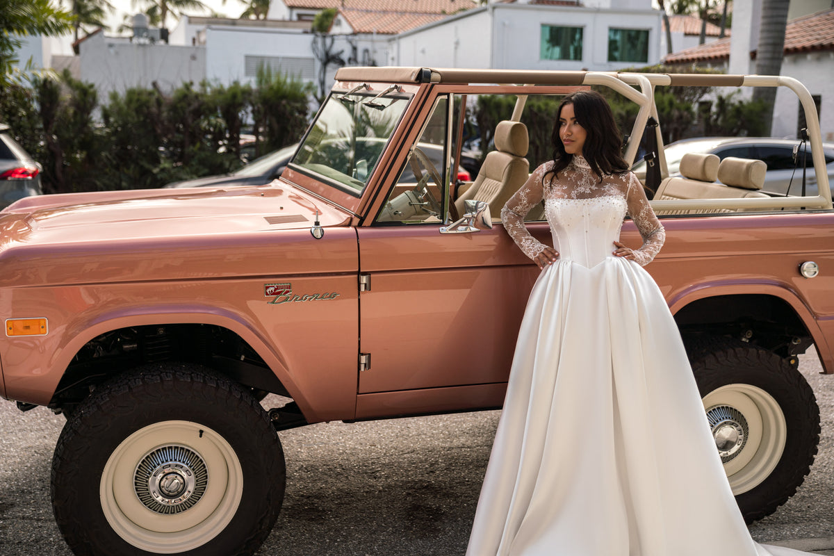 White wedding dress featuring a structured corset bodice, sheer lace sleeves, and a dramatic full-length ball-gown skirt