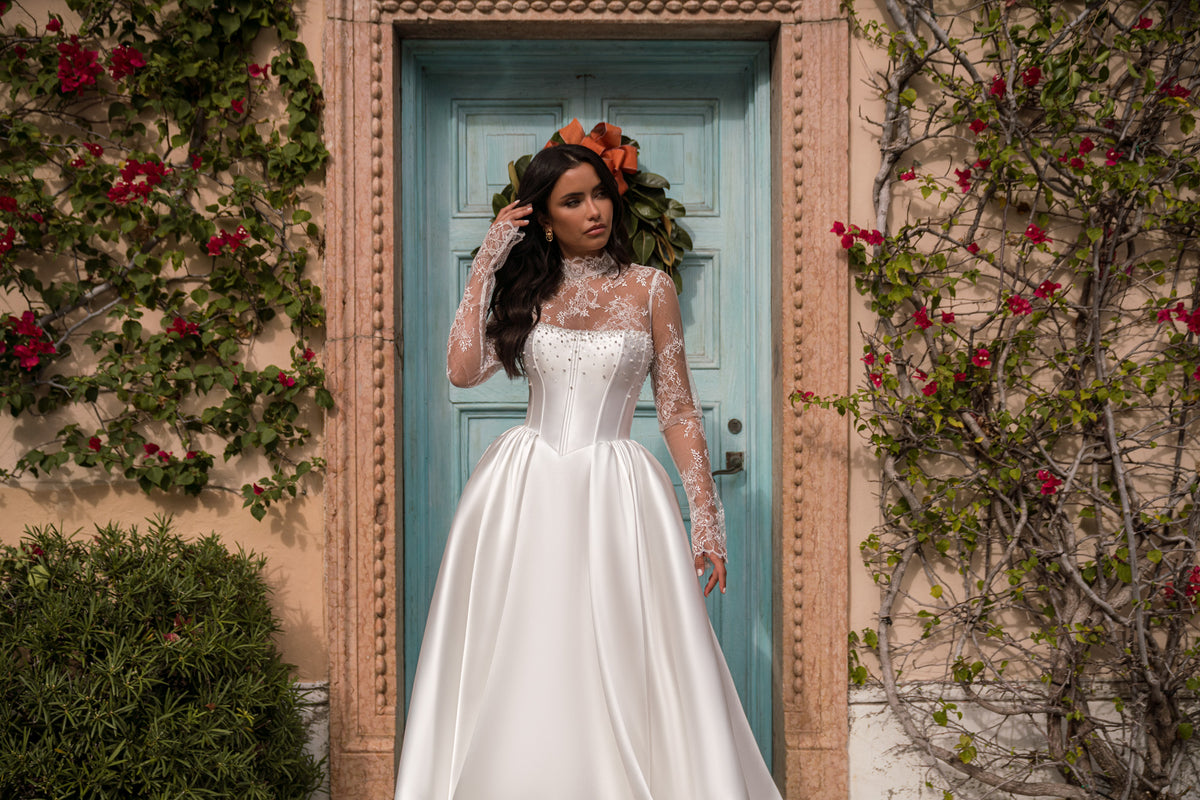 White wedding dress with a high lace neckline, long sheer sleeves, corset-style bodice, and gathered full skirt