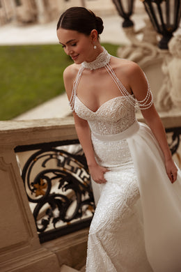Ivory wedding dress with a beaded sweetheart bodice, delicate shoulder chains, and a flowing overskirt