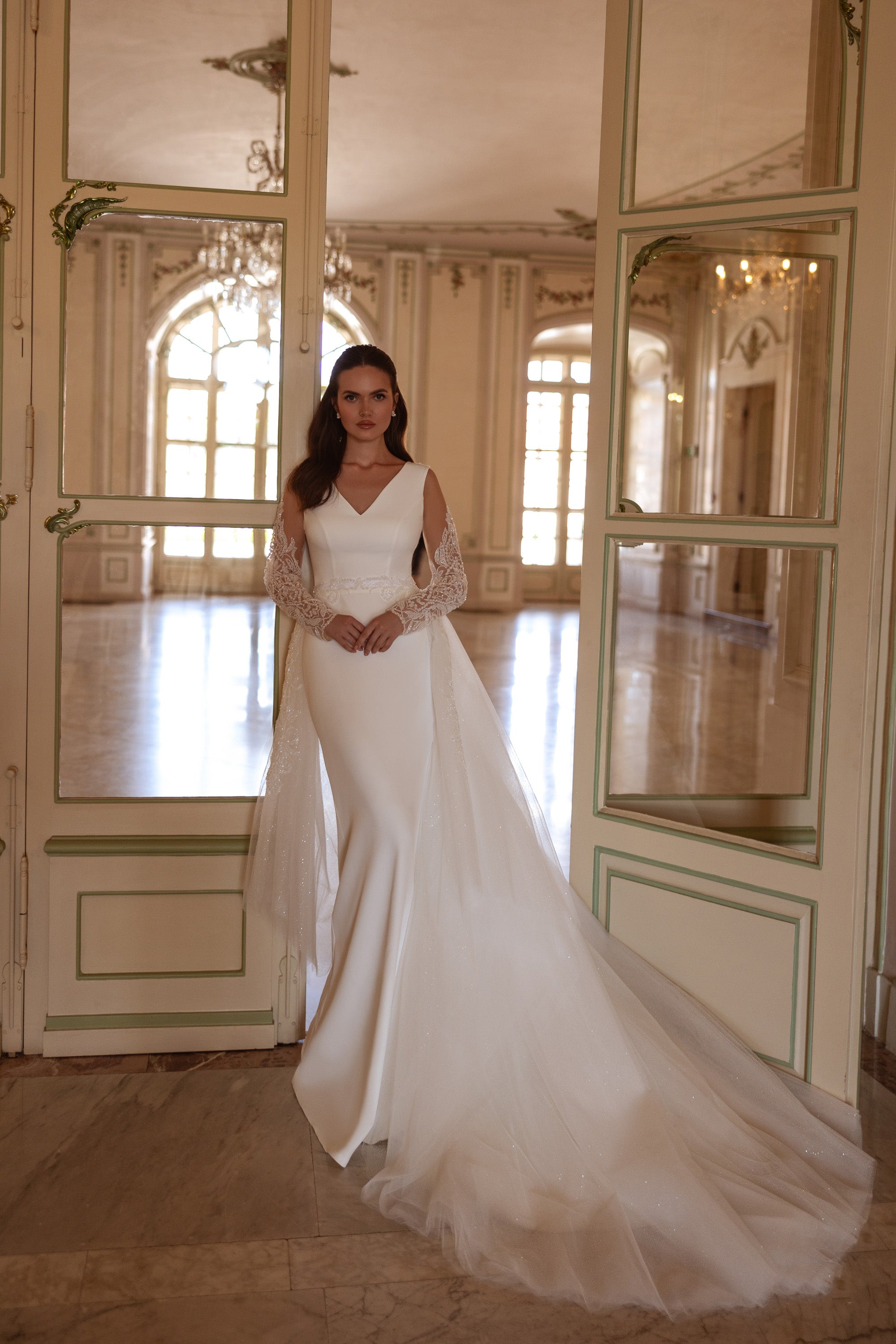 Ivory wedding dress with a V-neckline, long lace sleeves, fitted bodice, and flowing overskirt