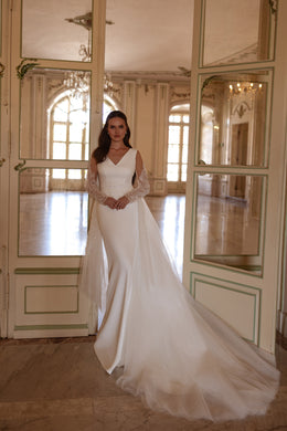 Ivory wedding dress with a V-neckline, long lace sleeves, fitted bodice, and flowing overskirt