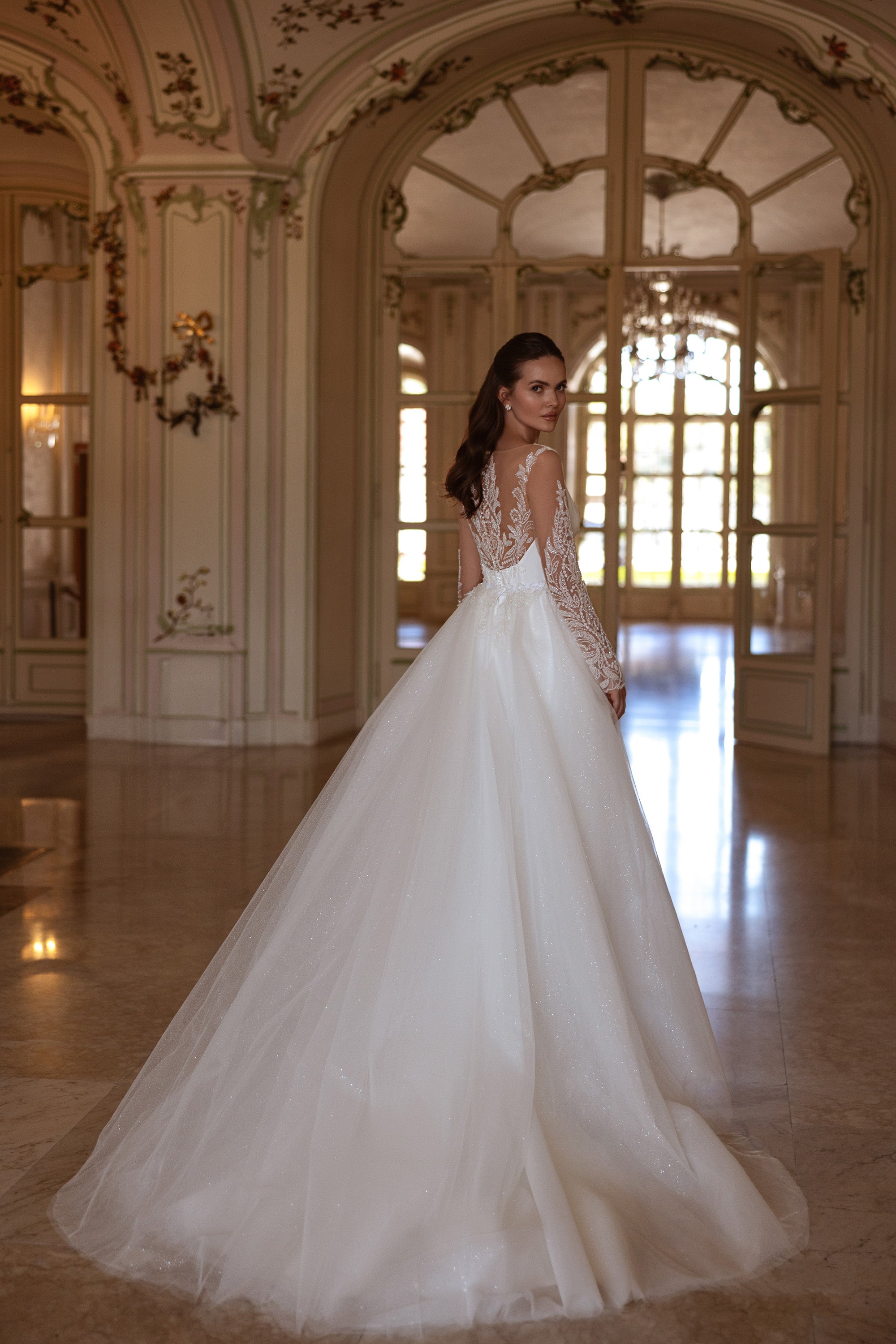 Wedding dress with an ornate illusion lace back, long sleeves, and a full glittering overskirt