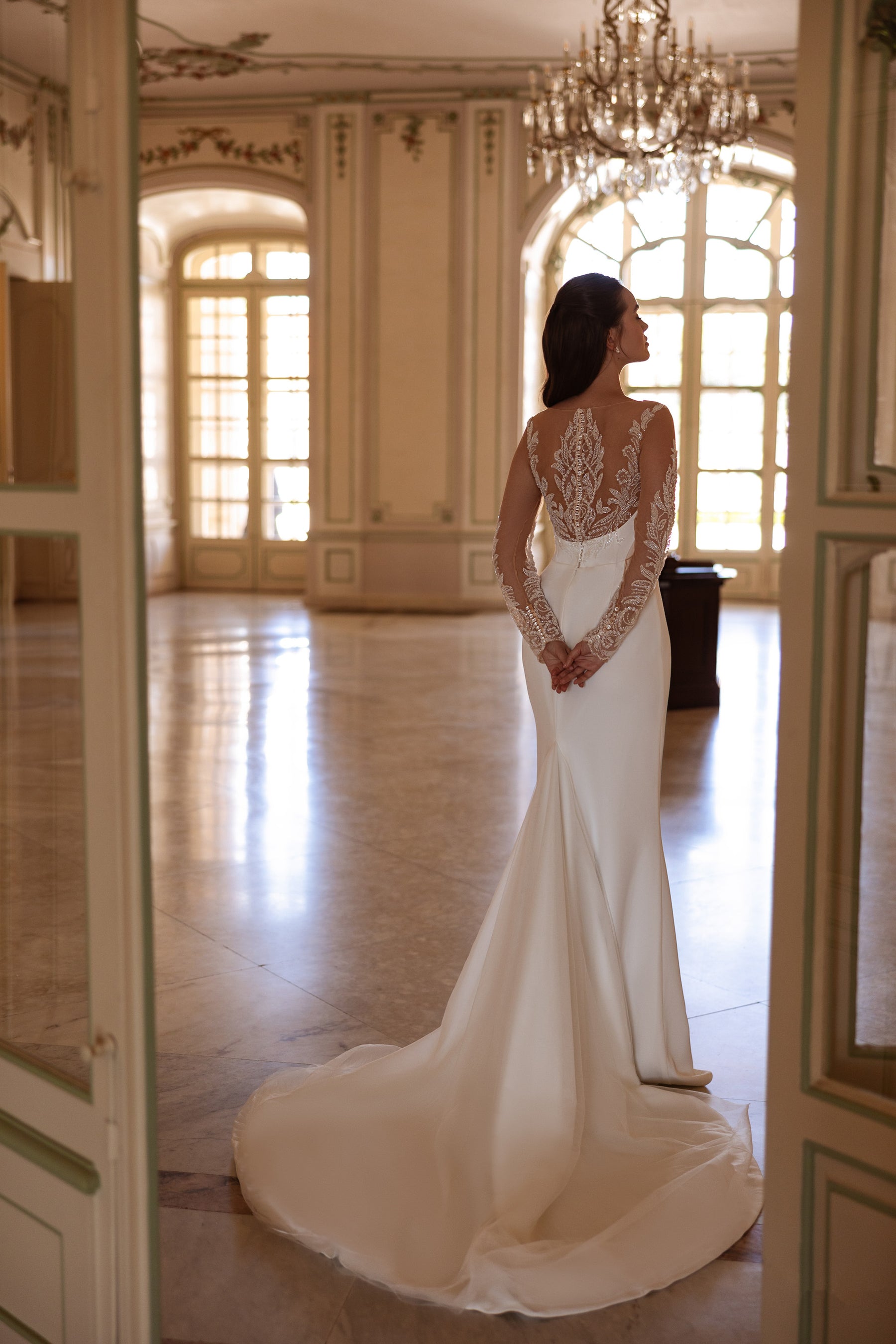 Open illusion lace back and fitted sheath silhouette with a long train on an ivory wedding dress