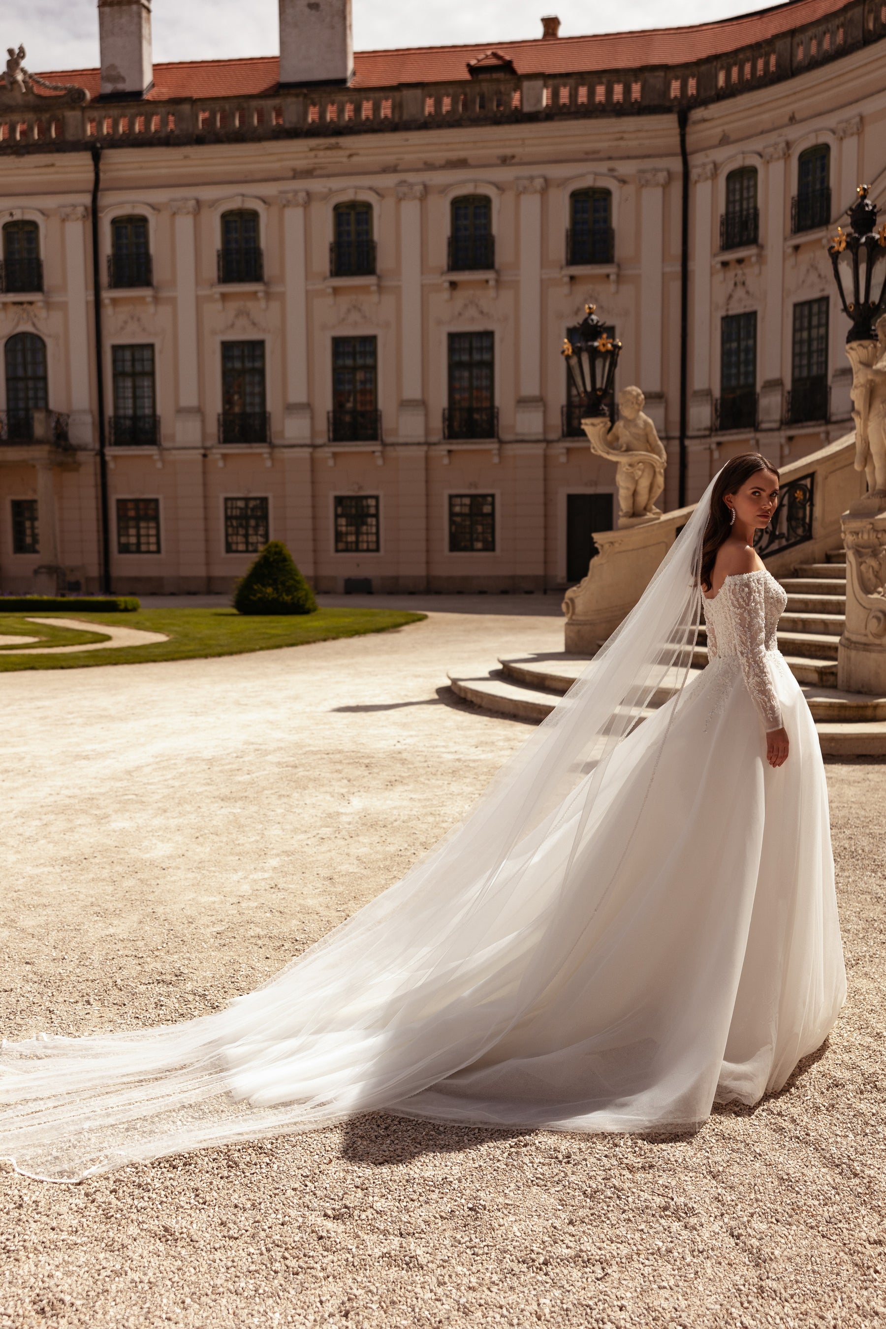 Side view of an ivory wedding dress with off-the-shoulder lace sleeves, a full skirt, and an extended train