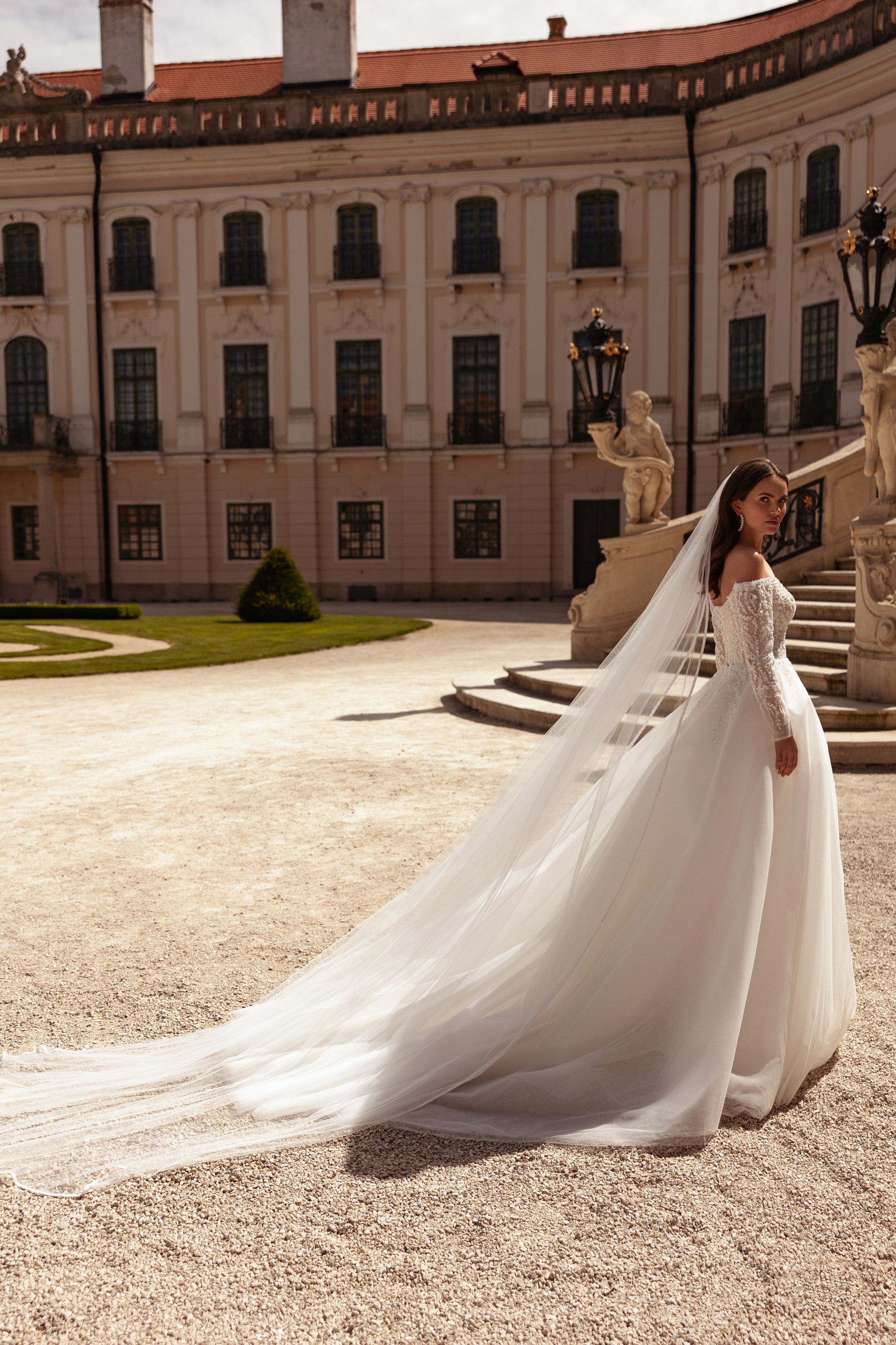 Side view of an ivory wedding dress with off-the-shoulder lace sleeves, a full skirt, and an extended train