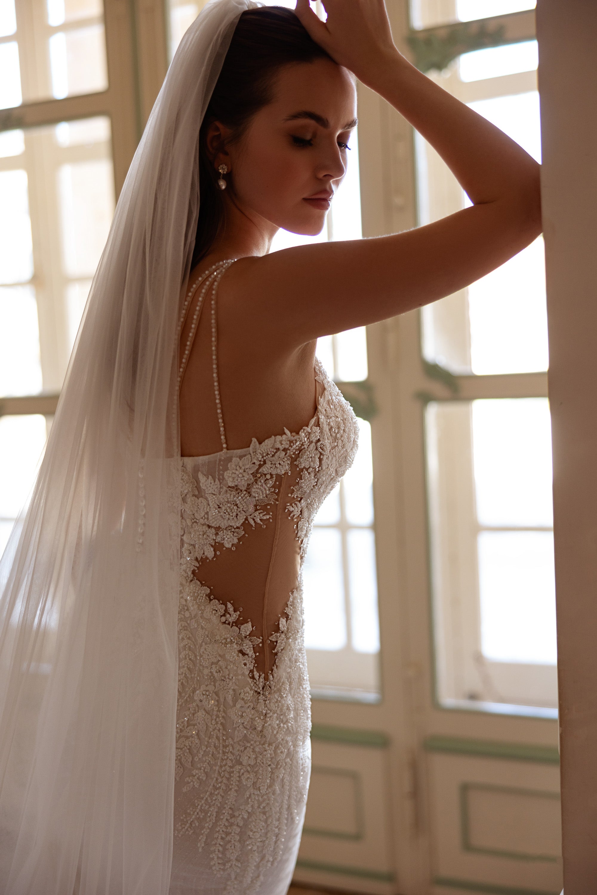 Side view of an ivory wedding dress with beaded lace, double shoulder straps, and a sheer illusion side panel